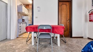 Uma pequena área de refeições com uma mesa coberta por toalha vermelha, duas cadeiras e uma porta de madeira.