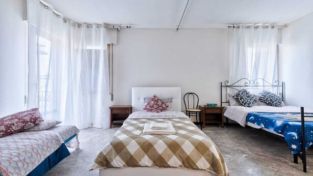 Quarto com duas camas de solteiro, uma cama grande no centro e uma cadeira.