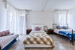 Une chambre avec deux lits simples, un grand lit au centre et une chaise.