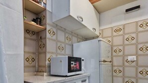 Uma cozinha compacta com micro-ondas, geladeira e um pequeno armário com prateleiras.