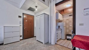 Quarto compacto com cozinha compacta, porta de madeira, armário branco e mesa vermelha.