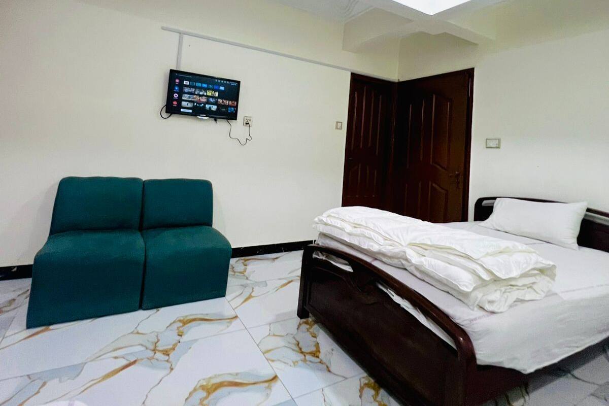 Habitación de hotel con cama, sofá verde, televisor de pantalla plana montado en la pared y puerta de madera.