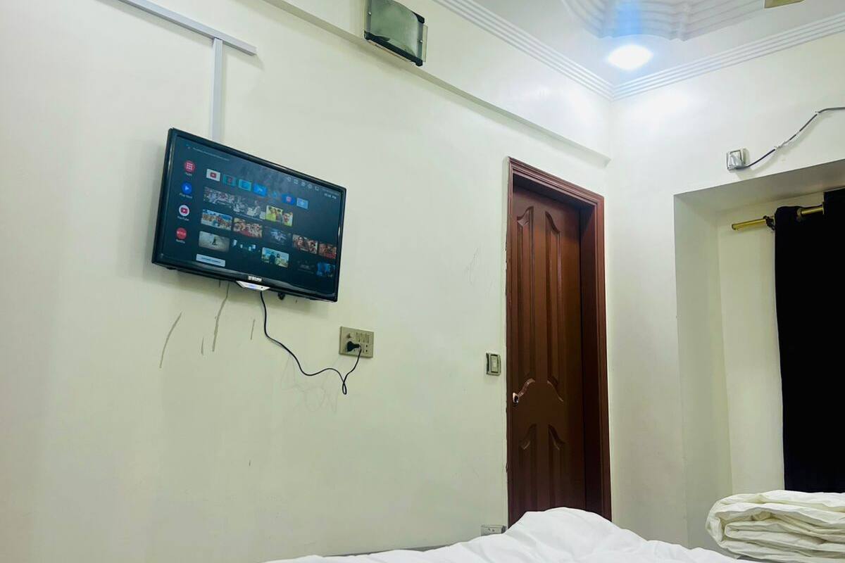 Un dormitorio con una cama, ventilador de techo, televisor montado y una puerta.