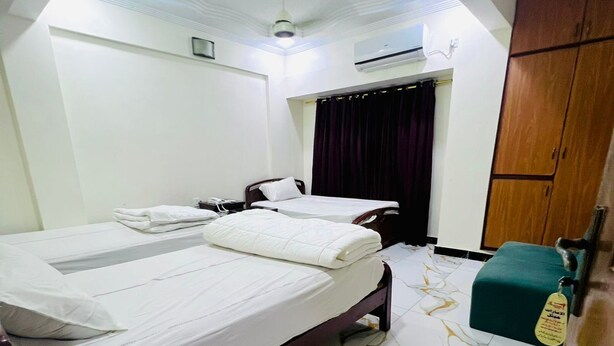 A hotel room with a large bed, a wooden wardrobe, and a marble-tiled floor. - Al Amarat Hotel Tariq Road (Karachi)