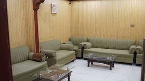 A living room with a green sofa set, a glass coffee table, and a wall-mounted air conditioner. - Al Amarat Hotel Tariq Road (Karachi)