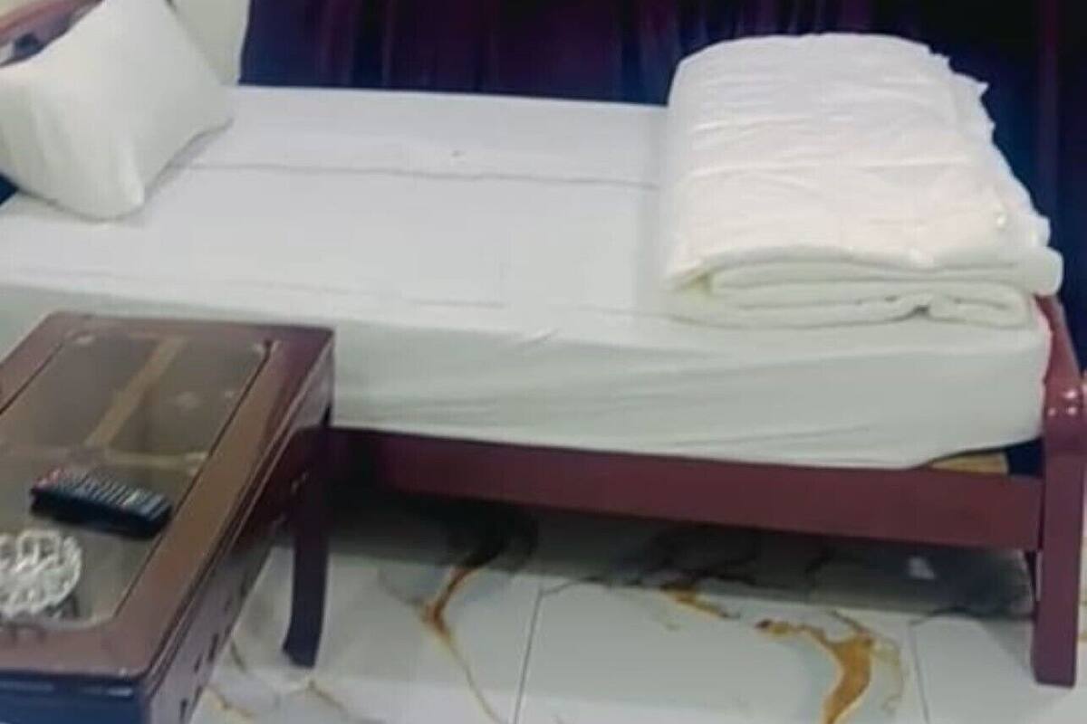 Una habitación pequeña con una cama individual, estructura de cama de madera, una mesita de noche con un control remoto y una cortina.