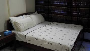 Un dormitorio con cama, almohadas, una mesita de noche y una caja de pañuelos, y una cortina.