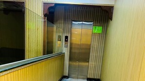 A narrow hallway with a marble floor, an elevator, and a door with a green sign. - Al Amarat Hotel Tariq Road (Karachi)