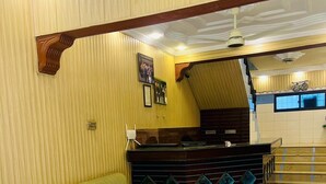A reception area with a green sofa, a reception desk, and a staircase leading to an upper floor. - Al Amarat Hotel Tariq Road (Karachi)