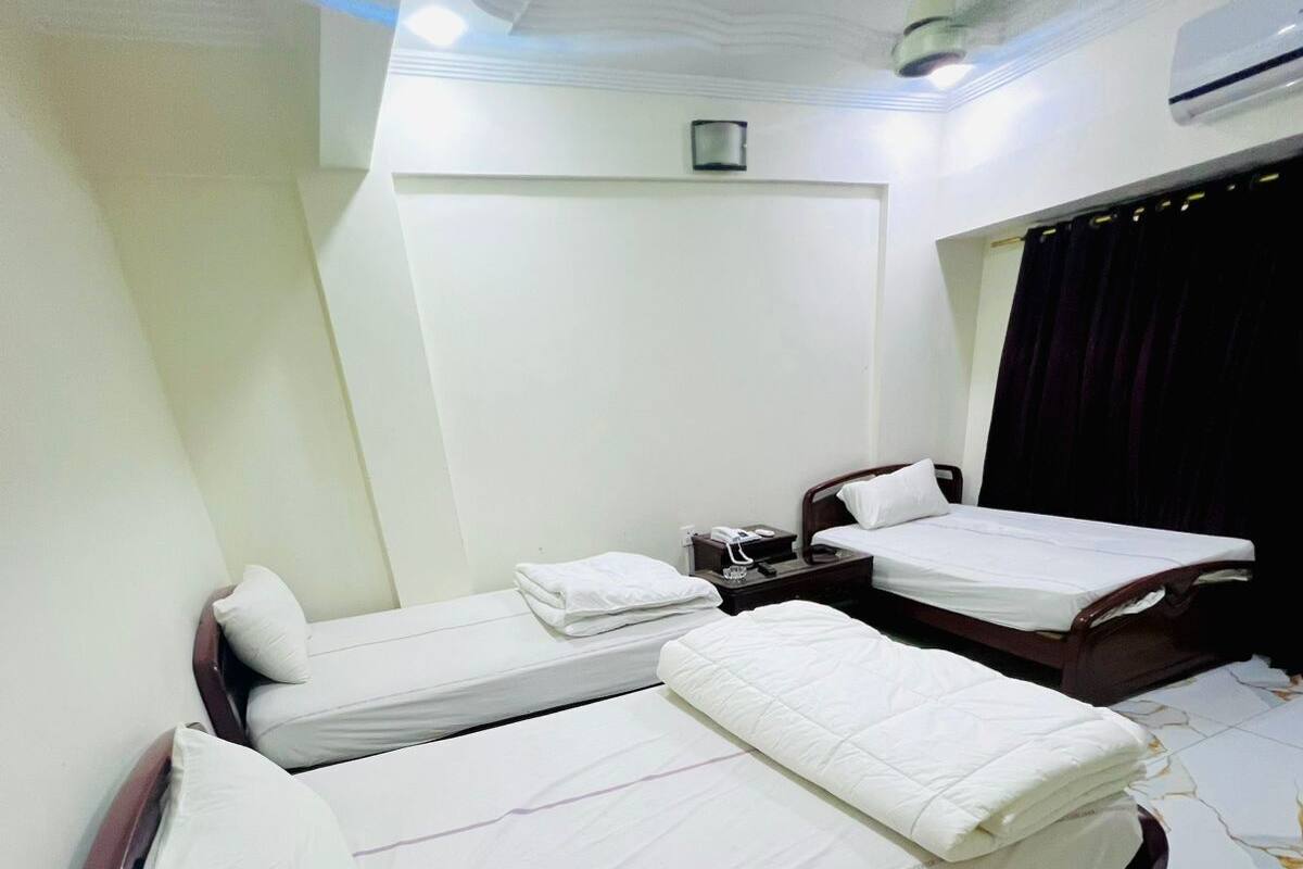 Habitación de hotel con dos camas individuales, una mesita de noche pequeña con lámpara, ventilador de techo y aire acondicionado de pared.