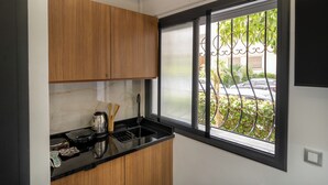 A kitchen with wooden cabinets, a black countertop, and a window with a view of a parked car and greenery outside. - Business & Chill Studio 3 minutes from the Grand Stade (Tanger)