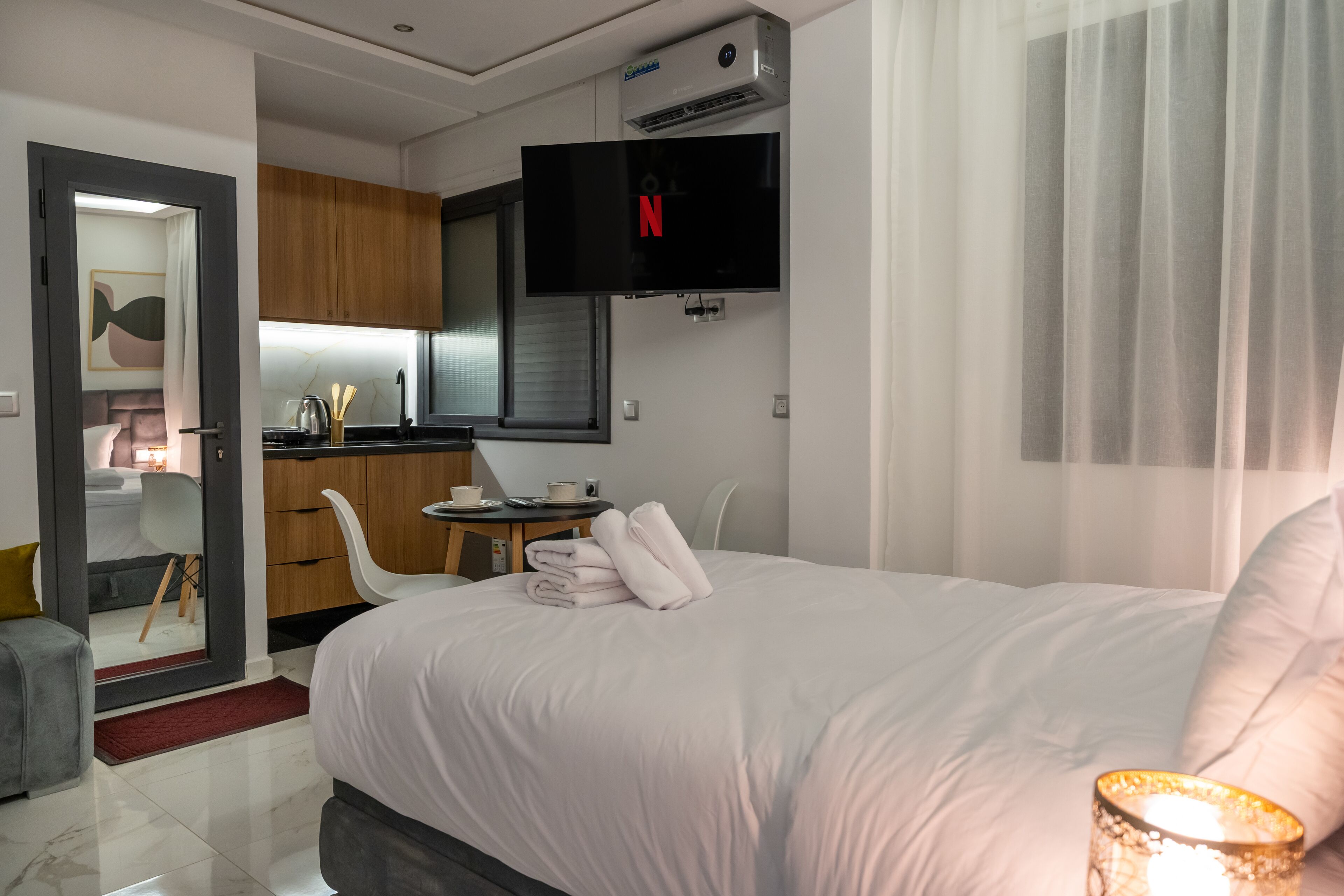 Ein Hotelzimmer mit einem Bett, einem an der Wand montierten Fernseher, einem kleinen Tisch mit Tasse und Teller sowie einer Küchenzeile.