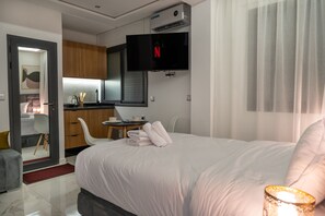 Hotelkamer met een bed, een aan de muur bevestigde televisie, een kleine tafel met een kopje en bord, en een kitchenette.