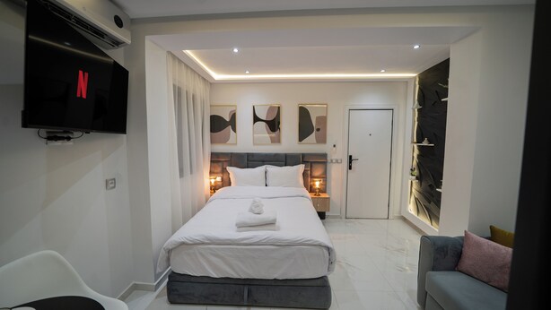 A modern hotel room with a large bed, a flat-screen TV mounted on the wall, a bedside table with a lamp, and a sofa with cushions. - Business & Chill Studio 3 minutes from the Grand Stade (Tanger)