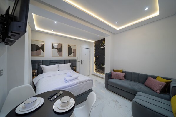 Een moderne hotelkamer met een groot bed, een grijze bank, een eettafel met borden en bestek, en abstracte muurkunst.