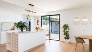 A modern kitchen with white cabinetry, a central island with a fruit bowl, and a dining area with a wooden table and chairs.