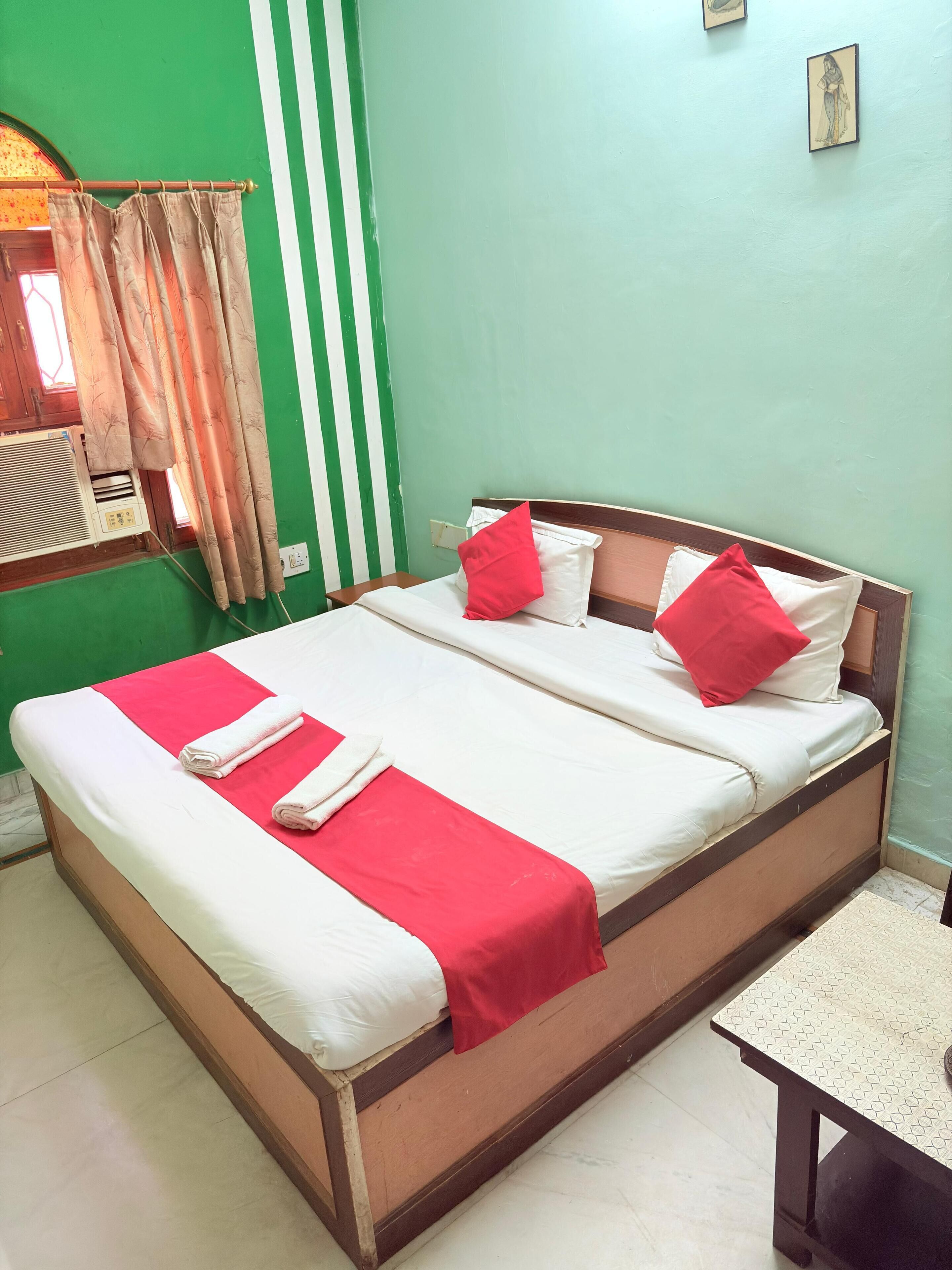 Uma cama bem arrumada com roupa de cama vermelha e branca, uma cabeceira de madeira e uma pequena mesa de cabeceira.