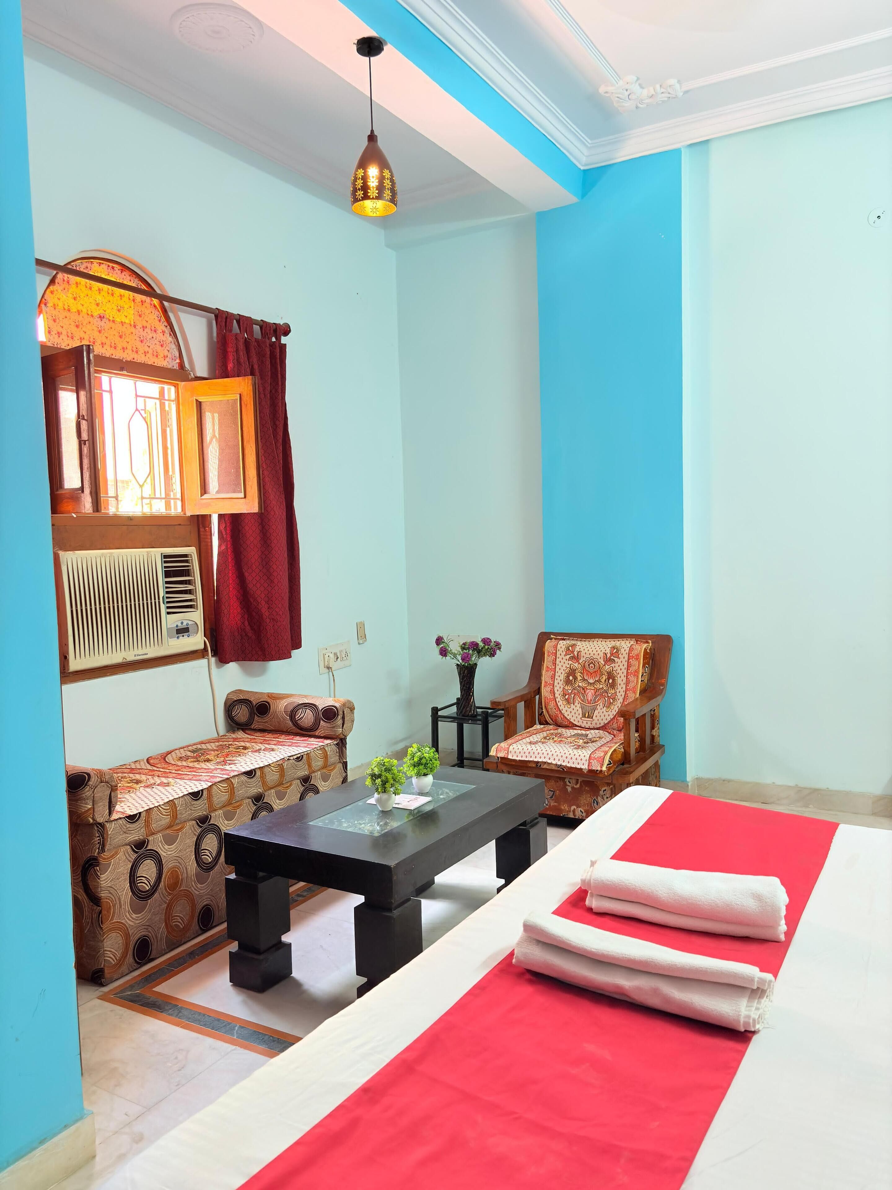 A room with a bed, two sofas, a small table, a decorative lamp, and a window with curtains.