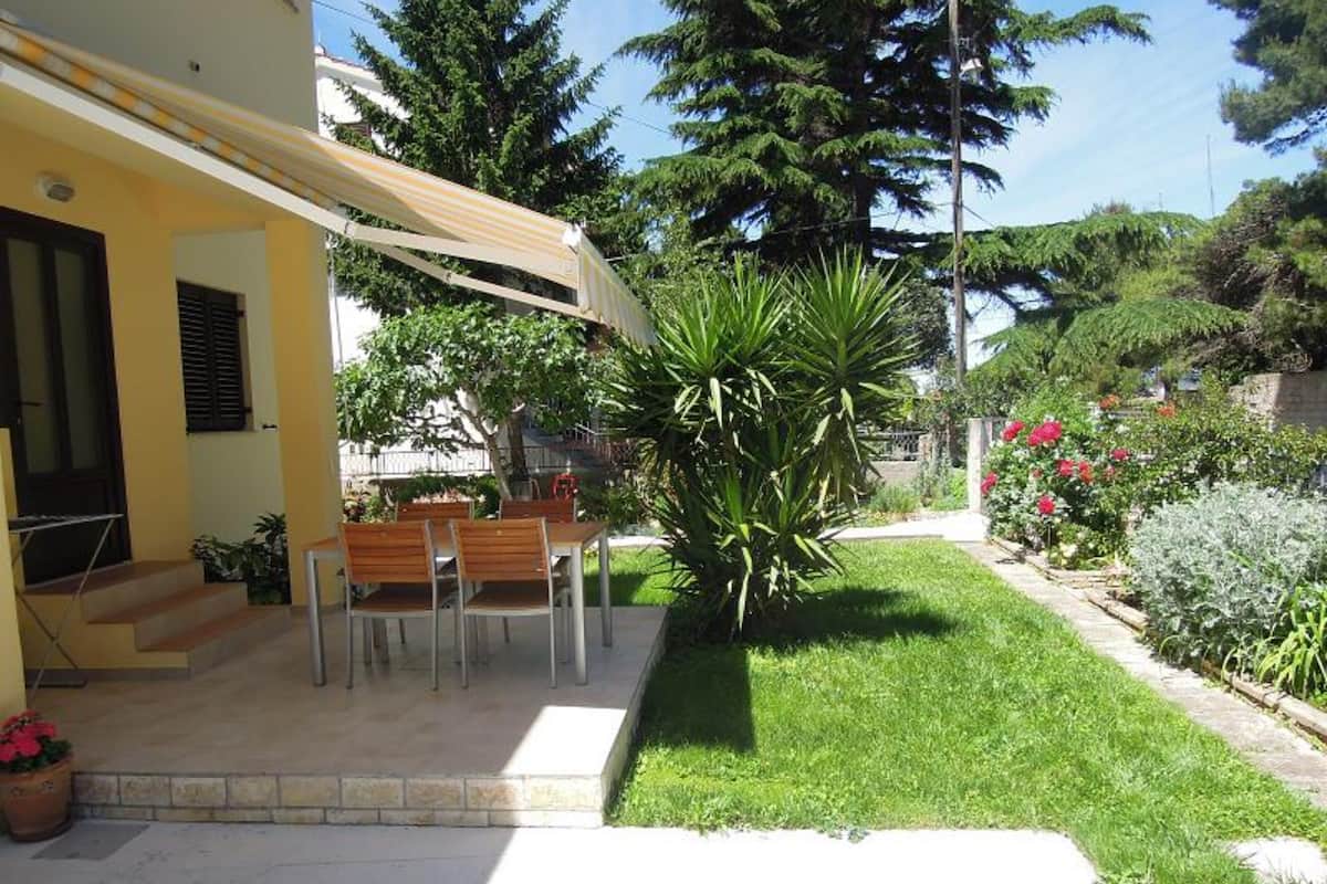 Ein Wohnhaus mit Terrasse, Sitzgelegenheiten im Freien, einem Rasen und verschiedenen Pflanzen.