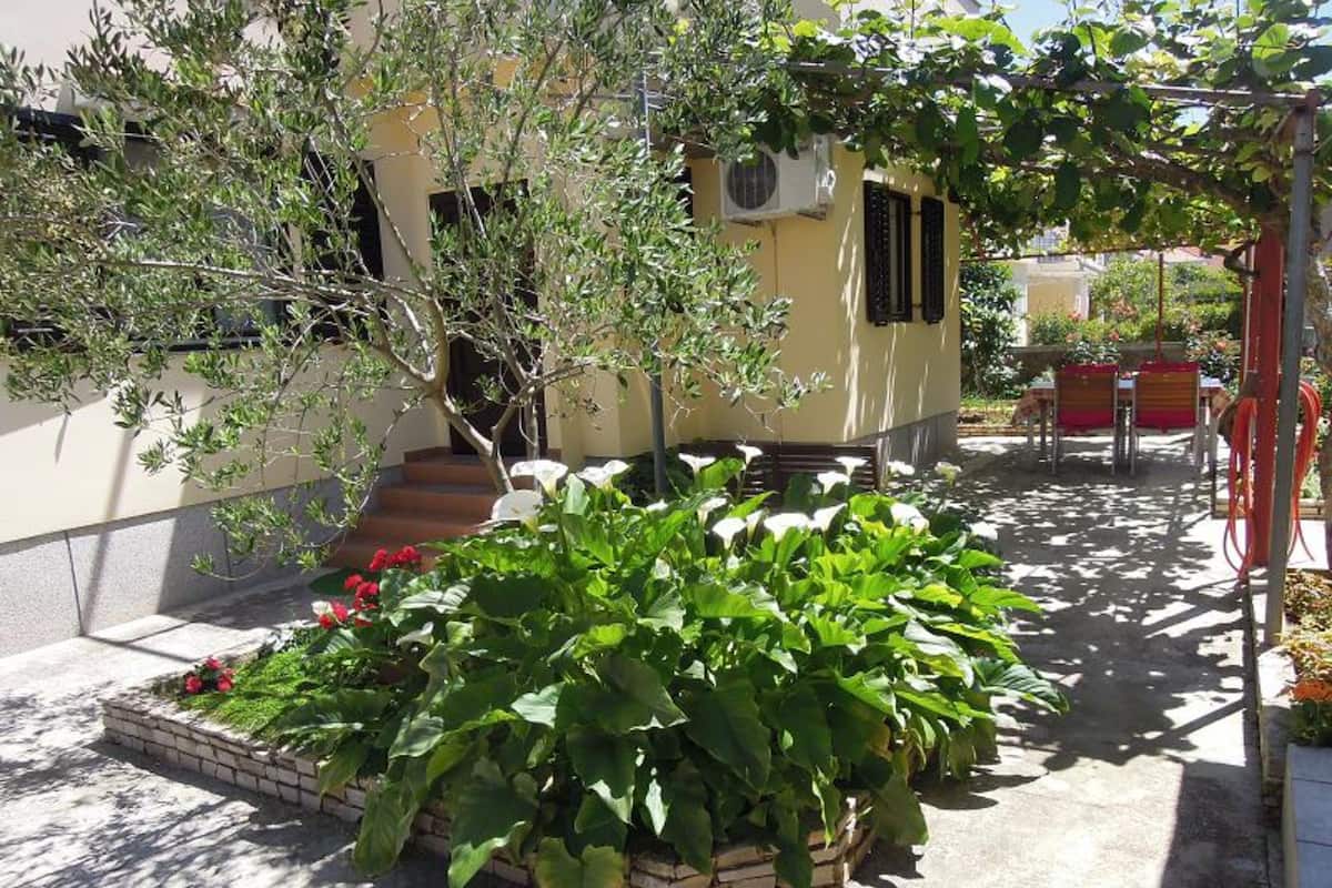 Ein Innenhof mit Blumenbeet, einem kleinen Baum und einem Gebäude mit Stufen, die zu einer Tür führen.