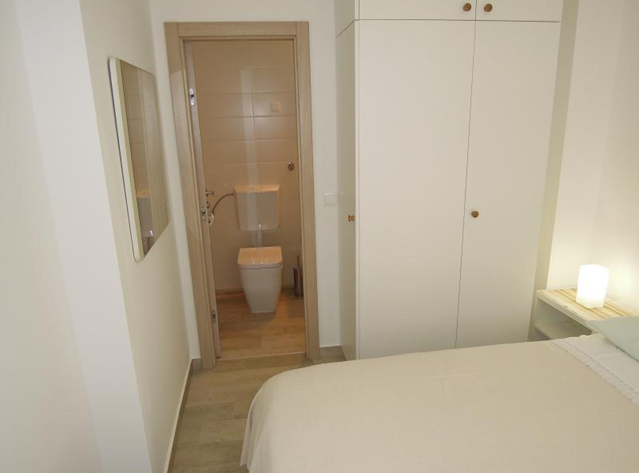 A bedroom with a bed, a wardrobe, and a toilet in the adjacent bathroom.