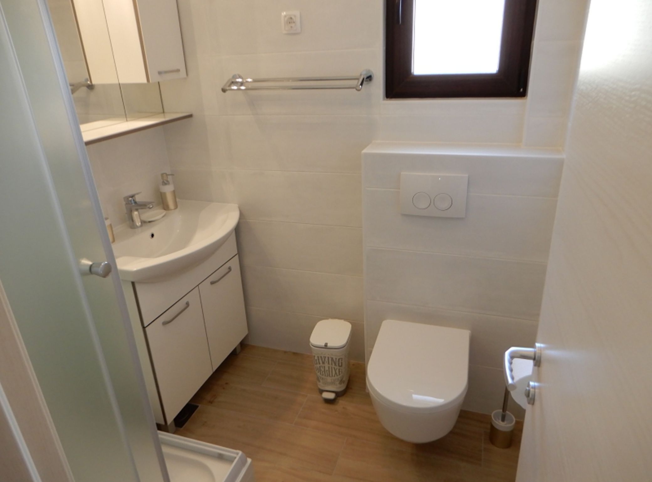 Et lille, rent badeværelse med en hvid vask, toilet og et lille vindue.