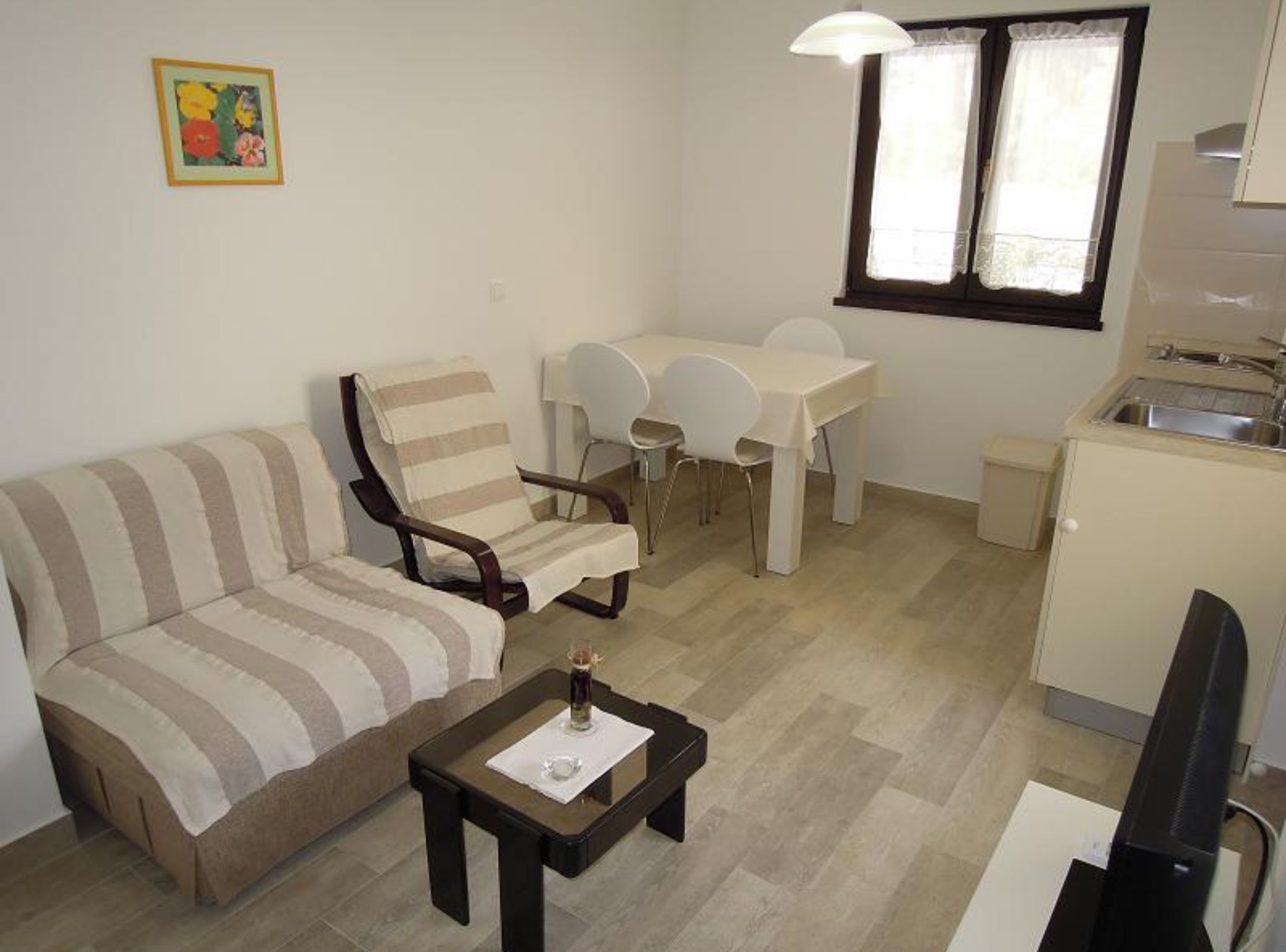Un espace de vie compact comprenant un canapé à rayures, une table à manger avec des chaises, un petit coin cuisine et une seule fenêtre.