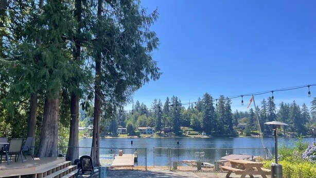 A lakeside patio with a wooden deck, outdoor seating, and a view of the lake and surrounding trees. - @ Marbella Lane - Nature Escape at Shady Lake (Renton)