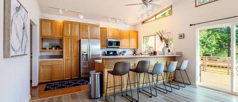 A modern kitchen with wooden cabinets, stainless steel appliances, and a bar area with bar stools.
