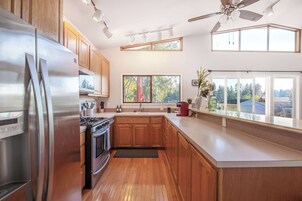 Una cocina moderna con armarios de madera, electrodomésticos de acero inoxidable y ventanas amplias que ofrecen vistas al exterior.