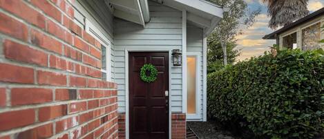 A house with a brick exterior, a dark wooden door with a green wreath, and a small porch area.