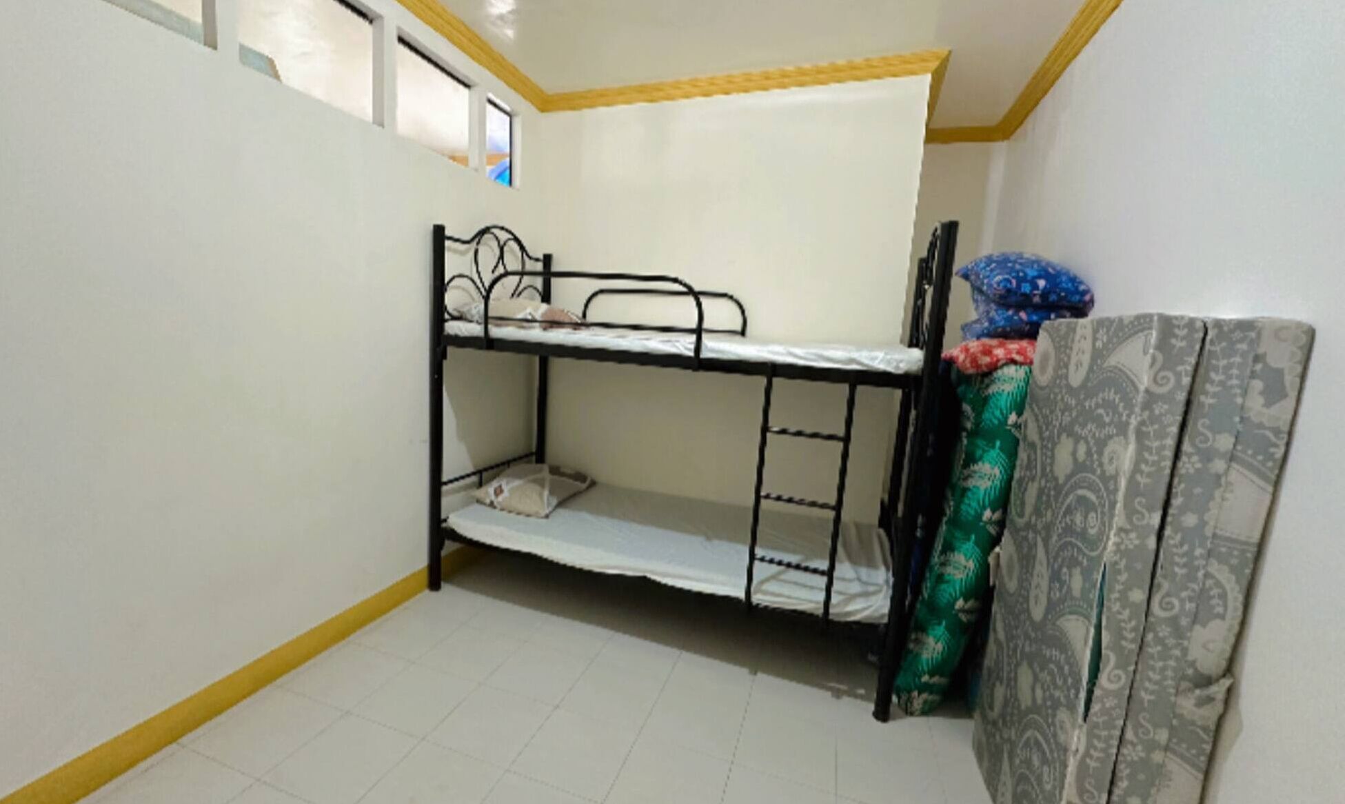 A small, single-bunk room with a window, a bed, and a mattress on the floor.