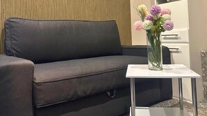 Un canapé gris foncé, avec une table en verre placée à côté, sur laquelle se trouve un vase rempli de fleurs.