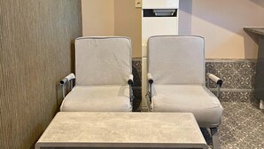 Un espace détente avec deux fauteuils confortables et une petite table, une imprimante fixée au mur, des carreaux de sol à motifs et une moquette verte à texture particulière.