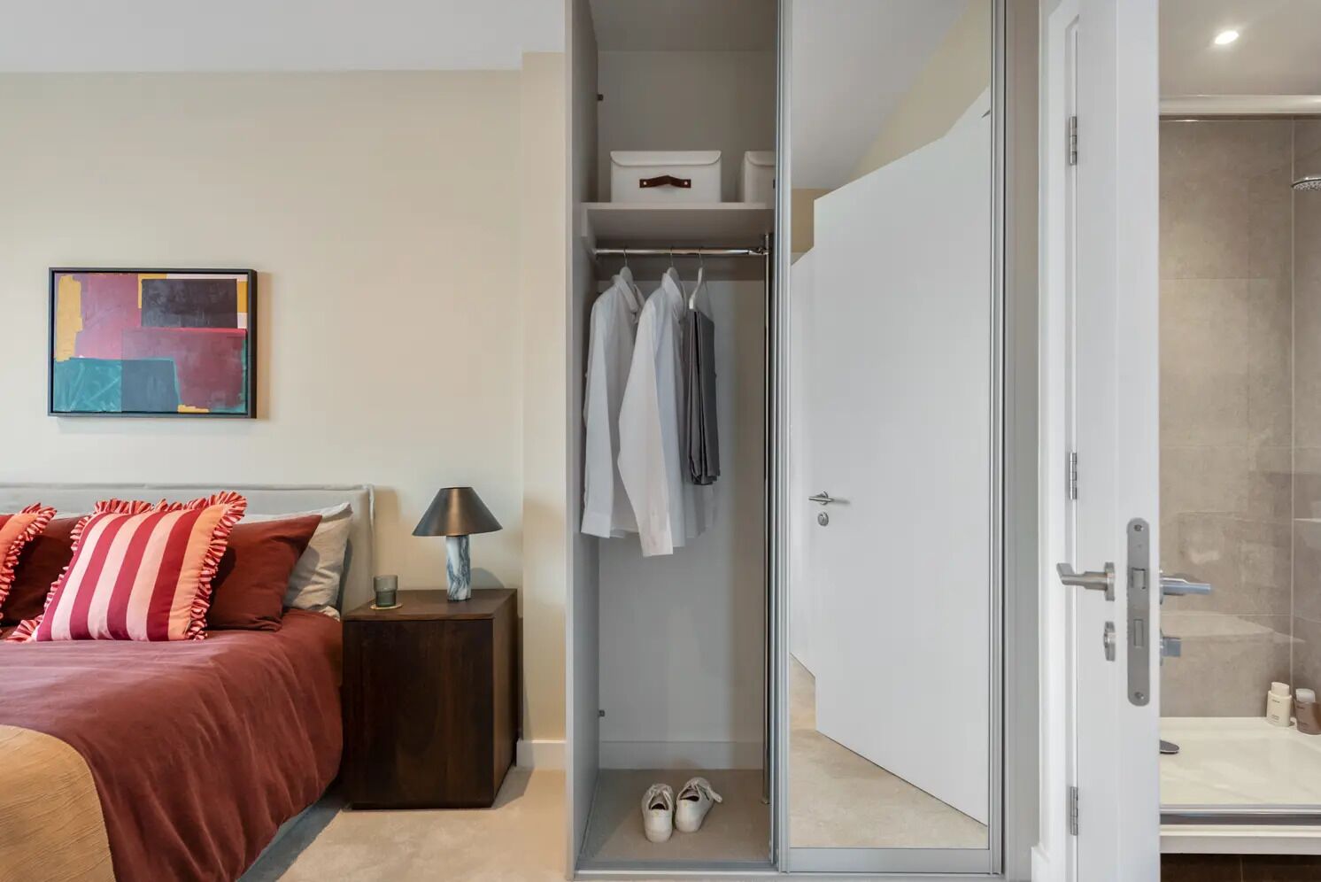 A modern bedroom with a bed, bedside table, and a walk-in closet with hanging clothes and shoes.