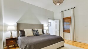 Een slaapkamer met een groot bed, twee nachtkastjes met lampen, een deur en een raam met gordijnen.