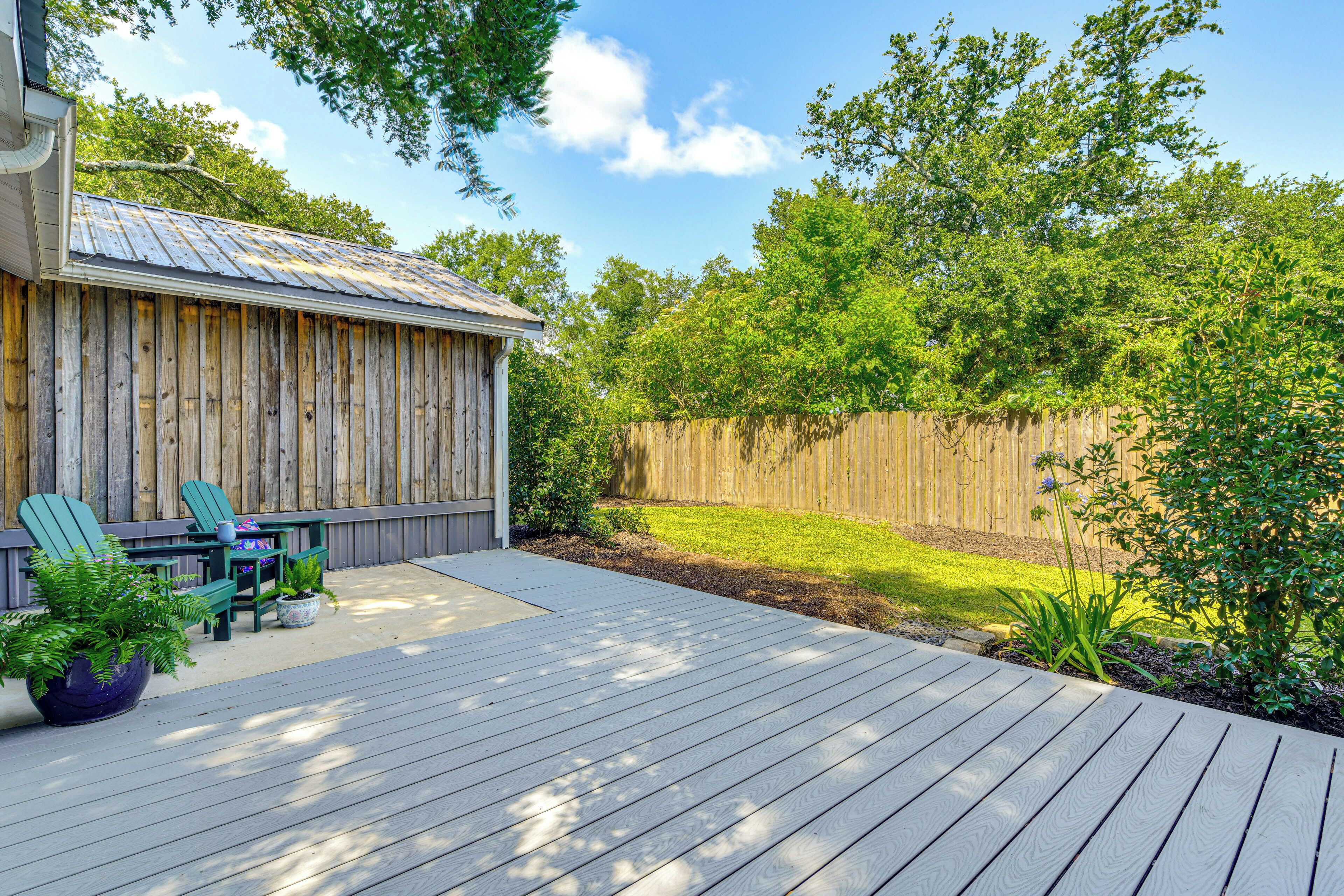 Une terrasse en bois, agrémentée de chaises et d’une table, entourée d’une clôture en bois et de verdure.