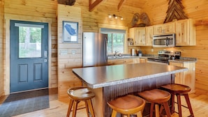 Ein Interieur einer Holzhütte mit einer Küche, die eine große Kochinsel, Barhocker, einen Kühlschrank und eine Mikrowelle umfasst.