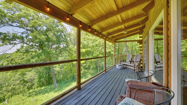 Eine Holzterrasse mit Stühlen und einem Tisch, mit Blick auf ein bewaldetes Gebiet.