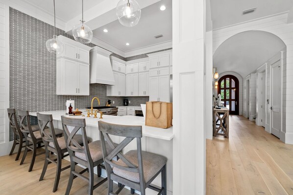 A modern kitchen with white cabinets, a central island, and a dining area with wooden chairs.