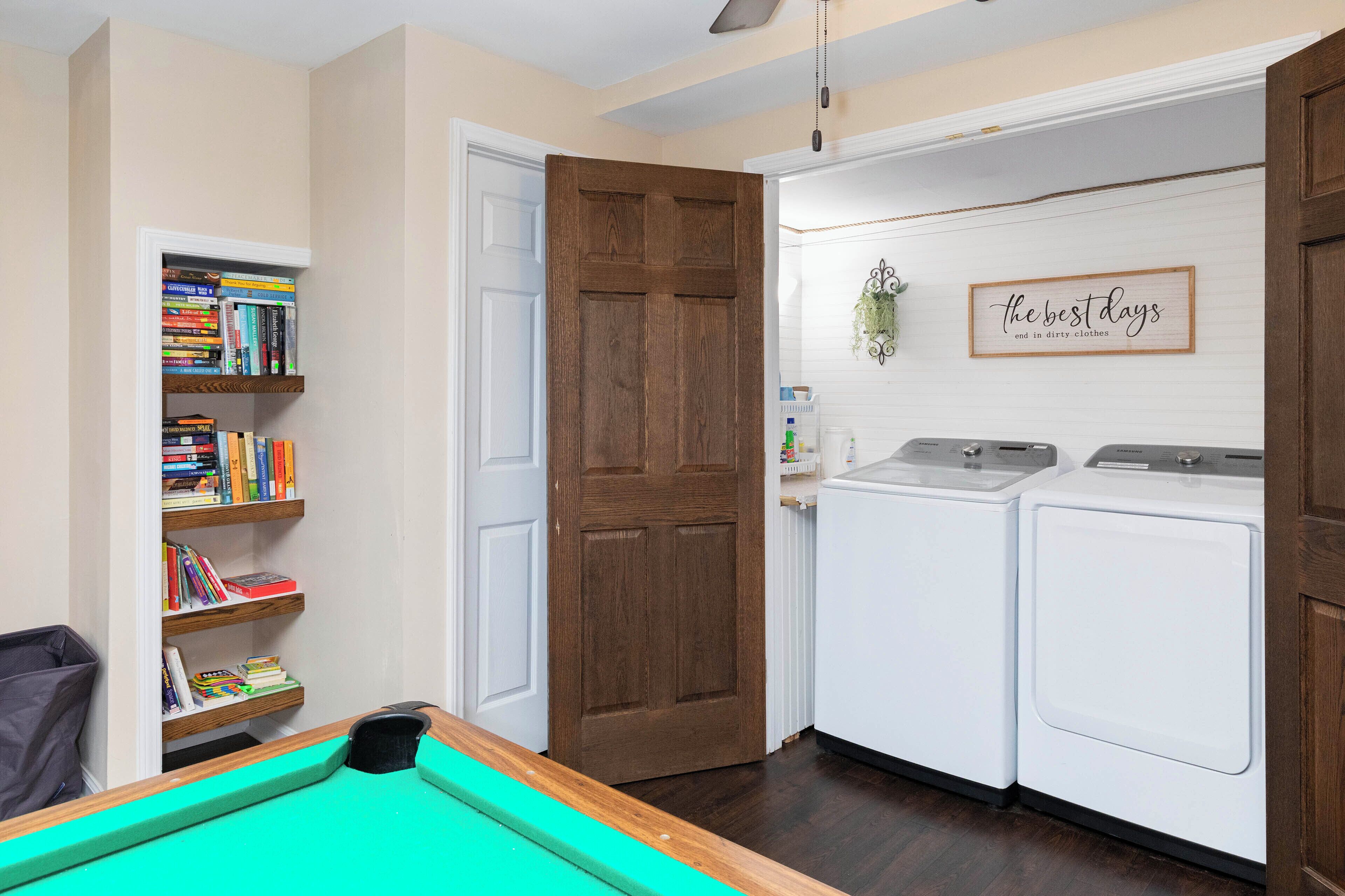 A laundry room with a door, two washing machines, and a shelf with books.