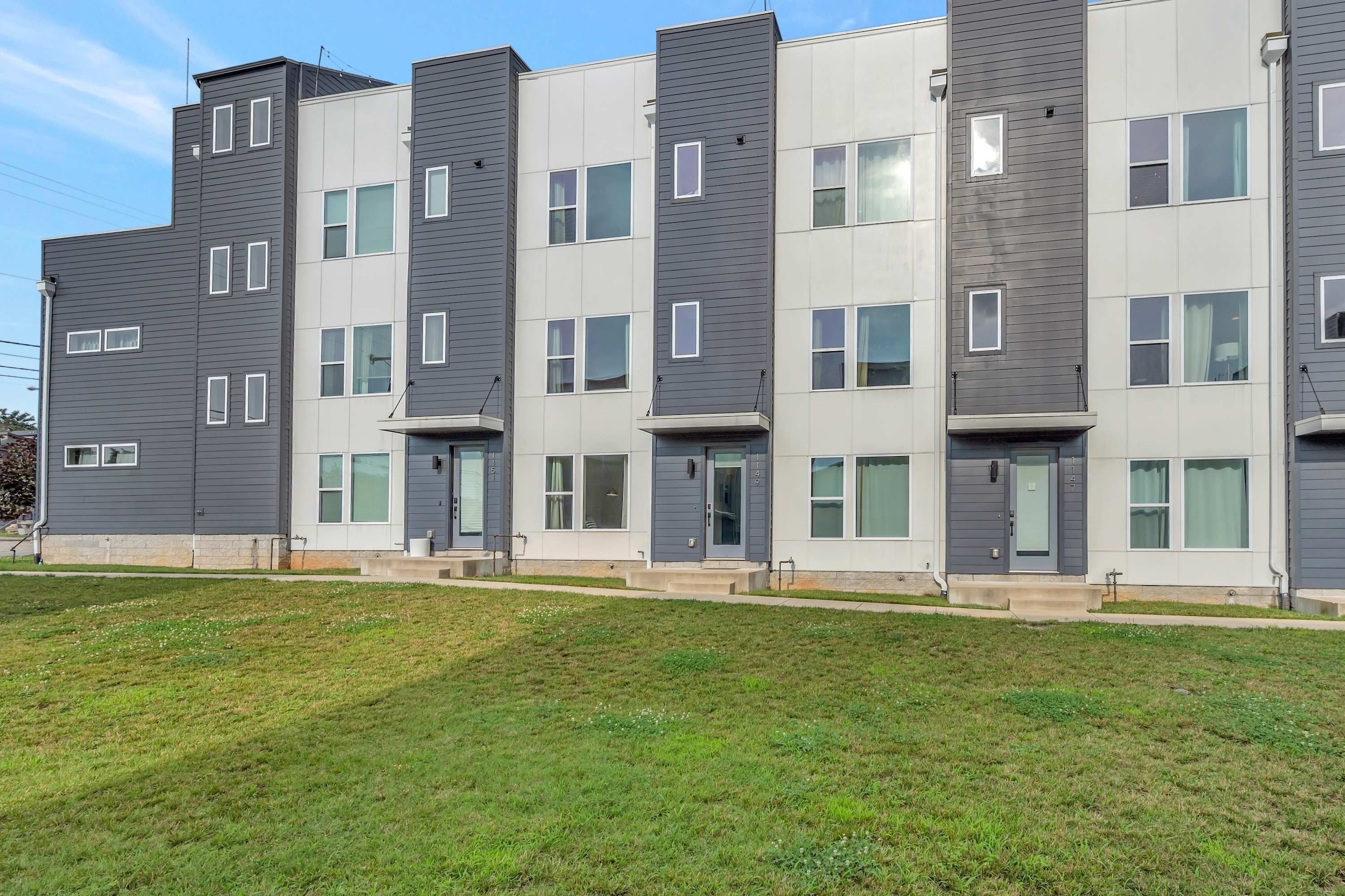 A multi-story residential building with a modern design, featuring a mix of dark and light-colored panels, multiple windows, and a flat roof.