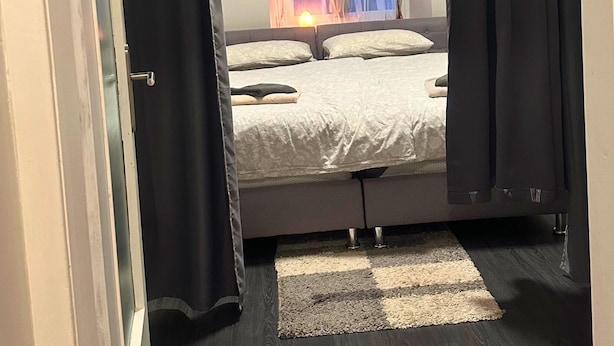 A bedroom with a bed, a window with curtains, a nightlight, and a checkered rug. - Apartment in Trier,mosl - Mosel (Pellingen)
