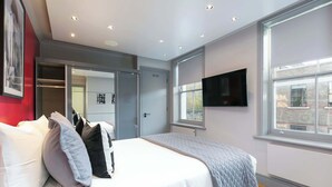 A modern bedroom with a large bed, a walk-in closet, a flat-screen TV, and a window with a city view. - The Georgian Wink Bloomsbury by Frankie Says (London)