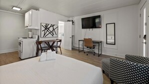 Una camera d'albergo con un letto, una scrivania, una sedia, una televisione e un angolo cottura.