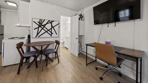 Una cucina moderna con mobili bianchi, un tavolo da pranzo con sedie, una TV a schermo piatto montata a parete e un piccolo angolo studio con scrivania e sedia.