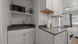 Una cucina compatta con mobili bianchi, un forno a microonde, un fornello e un lavello.