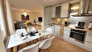 Une cuisine moderne avec des meubles blancs, un four encastré et un coin repas comprenant des chaises et une table blanches, le tout disposé pour deux personnes.