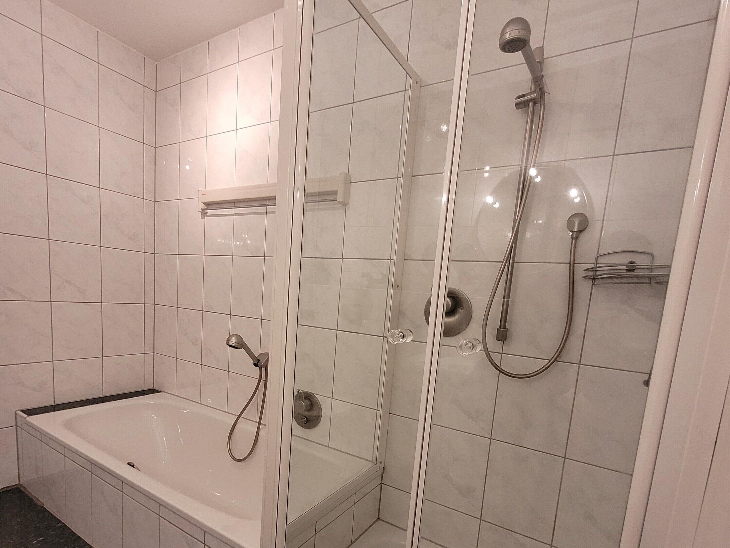 Une salle de bain moderne dotée d’une douche à parois de verre, d’une baignoire sur pied et de murs carrelés.