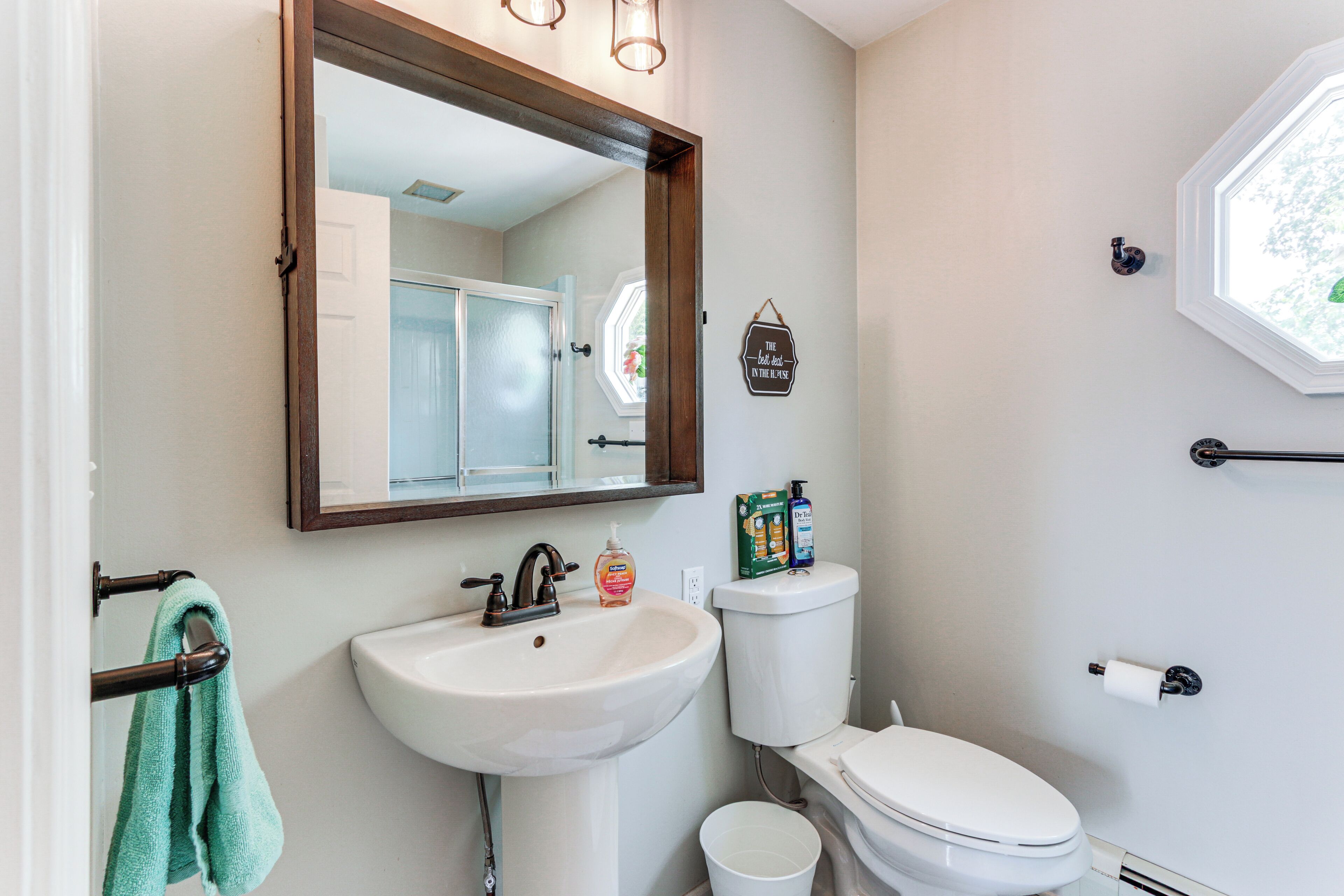 A bathroom with a white sink, a mirror, a toilet, and a window.